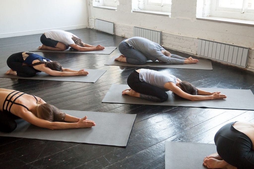 Group of young sporty people practicing in bikram yoga classes with instructor, lying in half tortoise pose