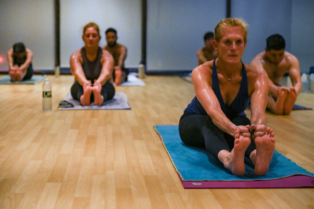 Bikram Yoga Class members in sit up pose with first two fingers around big toes