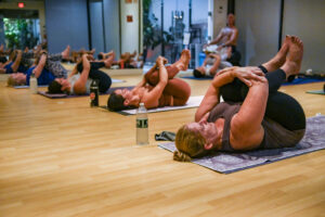 Bikram Yoga Class in Wind Removing Pose on backs with knees to chest
